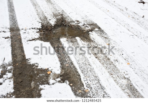 Car\
tire tracks and muddy road covered with fresh\
snow.
