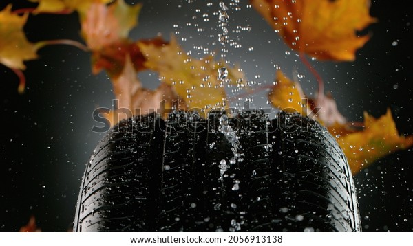 Car Tire with Water Splash and Autumn Leaves,\
Isolated on Black\
Background