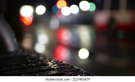 Car Traffic Lights Reflection On Bus Stop Bench In Rainy Weather. Water Rain Drops On Wet Metal, City Street In Clifornia, USA. Rainfall At Night. Defocused Abstract Close Up With Bokeh.