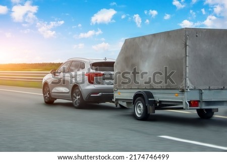 Car with a trailer covered with an awning is driving along the highway in the sky clouds and sunset