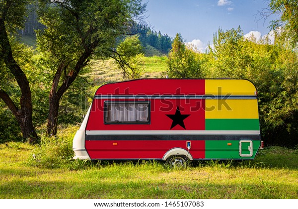 A car trailer, a motor home, painted in the national\
flag of Guinea Bisau stands parked in a mountainous. The concept of\
road transport, trade, export and import between countries. Travel\
by car