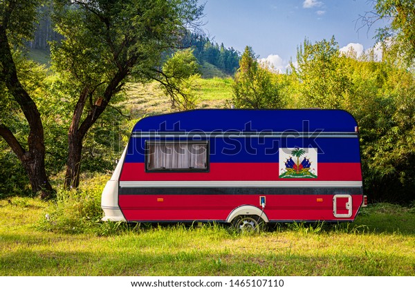 A car trailer, a motor home, painted in the national\
flag of Haiti stands parked in a mountainous. The concept of road\
transport, trade, export and import between countries. Travel by\
car