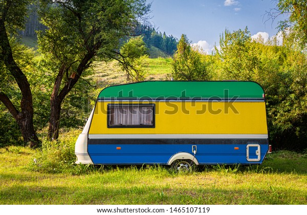 A car trailer, a motor home, painted in the national\
flag of Gabon stands parked in a mountainous. The concept of road\
transport, trade, export and import between countries. Travel by\
car