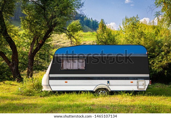 A car trailer, a motor home, painted in the national
flag of Estonia stands parked in a mountainous. The concept of road
transport, trade, export and import between countries. Travel by
car
