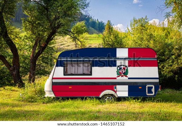 A car trailer, a motor home, painted in the national\
flag of Dominicana stands parked in a mountainous. The concept of\
road transport, trade, export and import between countries. Travel\
by car