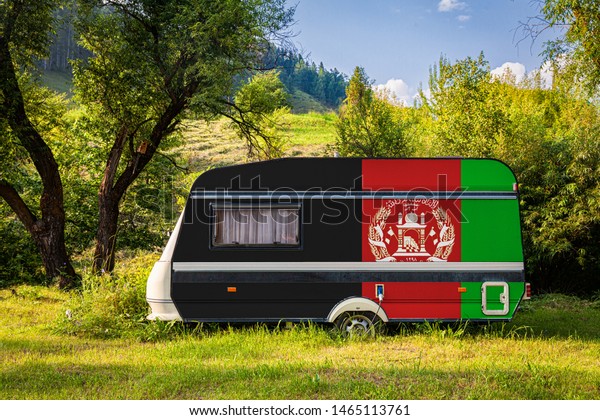 A car trailer, a motor home, painted in the national\
flag of Afghanistan stands parked in a mountainous. The concept of\
road transport, trade, export and import between countries. Travel\
by car