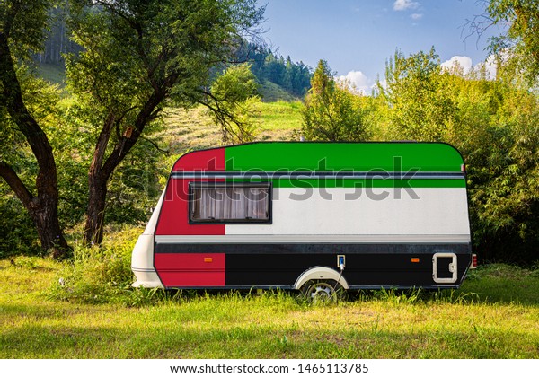 A\
car trailer, a motor home, painted in the national flag of United\
Arab Emirates stands parked in a mountainous. The concept of road\
transport, trade, export and import between countries.\

