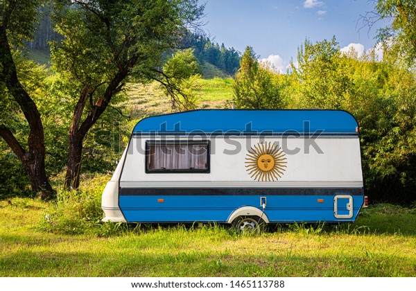 A car trailer, a motor home, painted in the national\
flag of Argentina stands parked in a mountainous. The concept of\
road transport, trade, export and import between countries. Travel\
by car