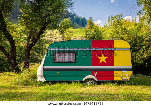 A car trailer, a motor home, painted in the national\
flag of Cameroon stands parked in a mountainous. The concept of\
road transport, trade, export and import between countries. Travel\
by car