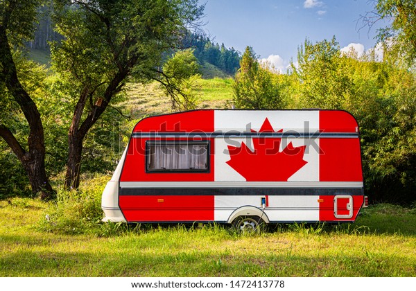A car trailer, a motor home, painted in the national\
flag of Canada stands parked in a mountainous. The concept of road\
transport, trade, export and import between countries. Travel by\
car