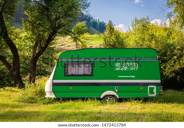 A car trailer, a motor home, painted in the national\
flag of Saudi Arabia stands parked in a mountainous. The concept of\
road transport, trade, export and import between countries. Travel\
by car