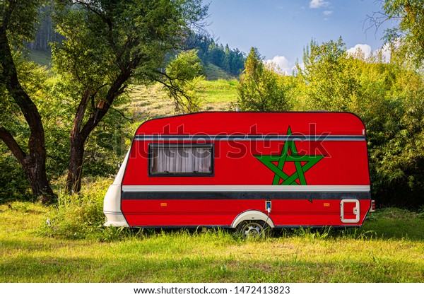 A car trailer, a motor home, painted in the national\
flag of Morocco stands parked in a mountainous. The concept of road\
transport, trade, export and import between countries. Travel by\
car