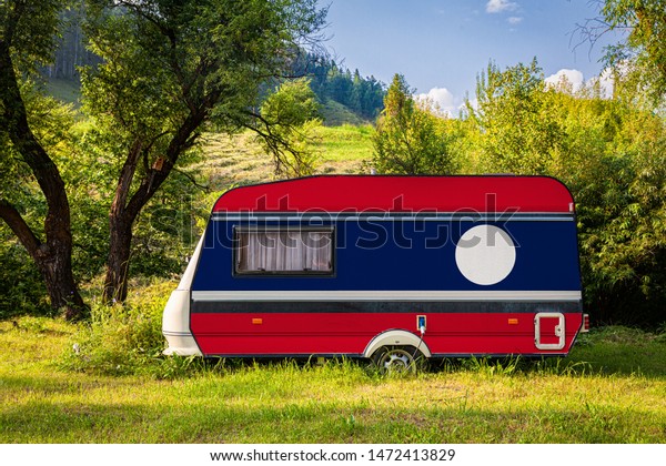A car trailer, a motor home, painted in the national\
flag of Laos stands parked in a mountainous. The concept of road\
transport, trade, export and import between countries. Travel by\
car