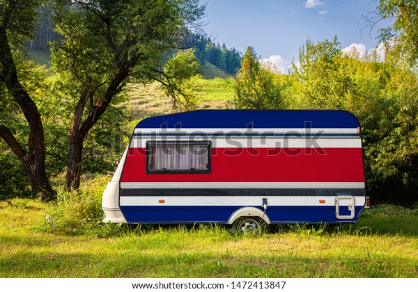 A car trailer, a motor home, painted in the national\
flag of Costa Rica stands parked in a mountainous. The concept of\
road transport, trade, export and import between countries. Travel\
by car