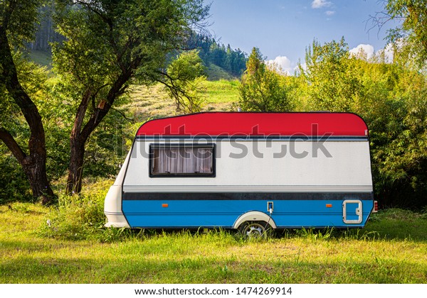 A car trailer, a motor home, painted in the national\
flag of  Luxembourg stands parked in a mountainous. The concept of\
road transport, trade, export and import between countries. Travel\
by car