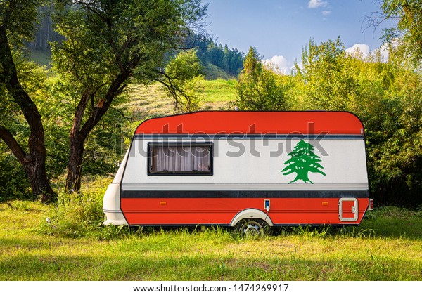 A car trailer, a motor home, painted in the national\
flag of  Lebanon stands parked in a mountainous. The concept of\
road transport, trade, export and import between countries. Travel\
by car