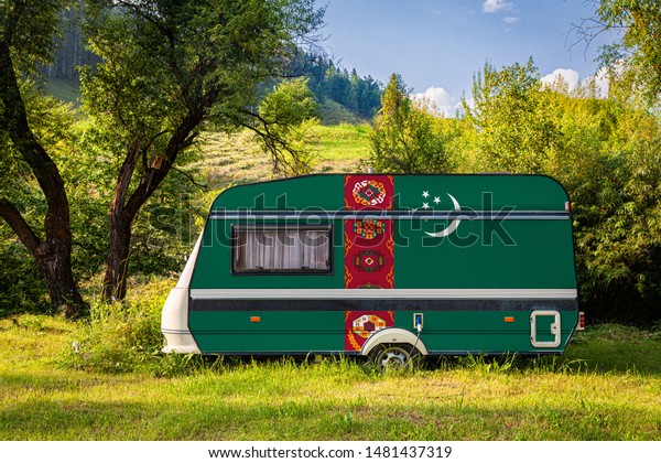 A car trailer, a motor home, painted in the national\
flag of  Turkmenistan stands parked in a mountainous. The concept\
of road transport, trade, export and import between countries.\
Travel by car