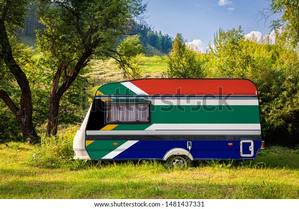 A car trailer, a motor home, painted in the\
national flag of  South African Republic stands parked in a\
mountainous. The concept of road transport, trade, export and\
import between countries.