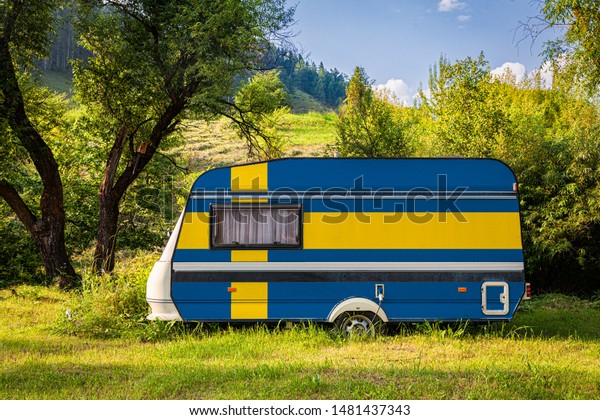 A car trailer, a motor home, painted in the national\
flag of  Sweden stands parked in a mountainous. The concept of road\
transport, trade, export and import between countries. Travel by\
car