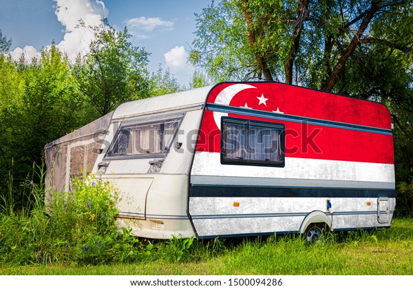 A\
car trailer, a motor home, painted in the national flag of \
Singapore stands parked in a mountainous. The concept of road\
transport, trade, export and import between\
countries.