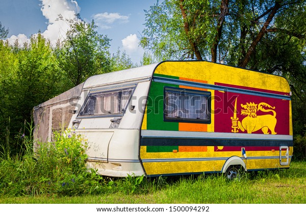 A\
car trailer, a motor home, painted in the national flag of  Sri\
Lanka stands parked in a mountainous. The concept of road\
transport, trade, export and import between\
countries.