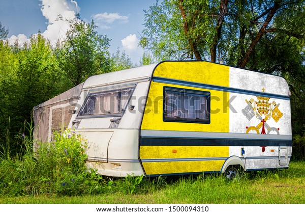 A car\
trailer, a motor home, painted in the national flag of  Vatican\
stands parked in a mountainous. The concept of road transport,\
trade, export and import between\
countries.