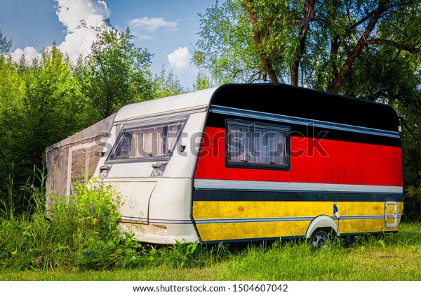 A car\
trailer, a motor home, painted in the national flag of  Germany\
stands parked in a mountainous. The concept of road transport,\
trade, export and import between\
countries.