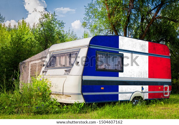 A car\
trailer, a motor home, painted in the national flag of  France\
stands parked in a mountainous. The concept of road transport,\
trade, export and import between\
countries.