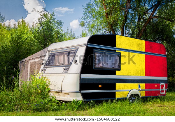 A car\
trailer, a motor home, painted in the national flag of  Belgium\
stands parked in a mountainous. The concept of road transport,\
trade, export and import between\
countries.