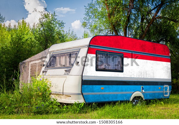 A\
car trailer, a motor home, painted in the national flag of \
Luxembourg\ stands parked in a mountainous. The concept of road\
transport, trade, export and import between\
countries.
