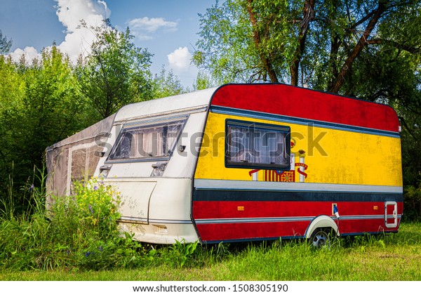 A car\
trailer, a motor home, painted in the national flag of  Spain\
stands parked in a mountainous. The concept of road transport,\
trade, export and import between\
countries.