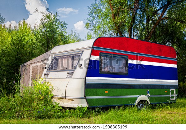 A car\
trailer, a motor home, painted in the national flag of  Gambia\
stands parked in a mountainous. The concept of road transport,\
trade, export and import between\
countries.