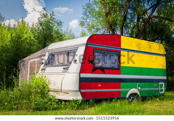 A\
car trailer, a motor home, painted in the national flag of  Guinea\
Bissau stands parked in a mountainous. The concept of road\
transport, trade, export and import between\
countries.