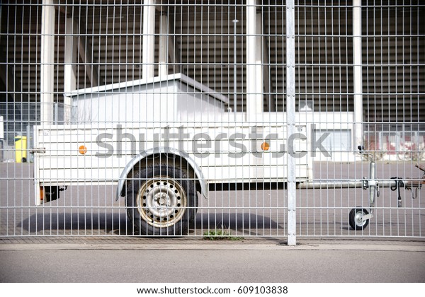 A car trailer for transporting small objects, tools and\
materials is parking behind a fence / Car trailer                  \
      