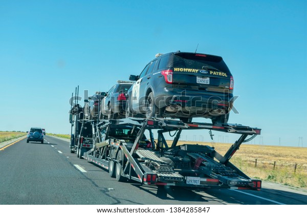 Car transporter carries California highway\
patrol cruisers along the highway, back view of the trailer - Lost\
Hills, California, USA - April 22,\
2019