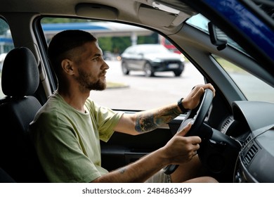 A car traveler is driving a car. The man refueled the car at the gas station and is ready to go further towards adventures. Side view portrait. Solo travel by car - Powered by Shutterstock