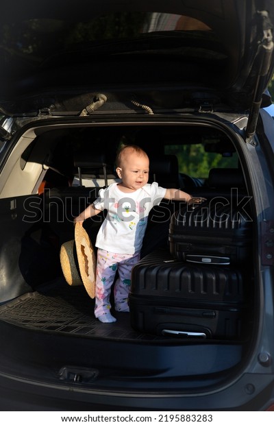 Car trip\
with a child. Open trunk of the car. Suitcases on the road. Baby\
with a traveler\'s hat. High quality\
photo