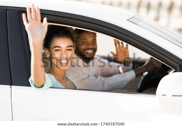 Car Trip. Happy African\
American Couple Waving Good Bye Sitting In Auto During Ride.\
Selective Focus