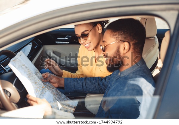 Car Trip.\
Happy Black Spouses Looking At Road Map Sitting In Car Traveling On\
Summer Vacation. Selective\
Focus