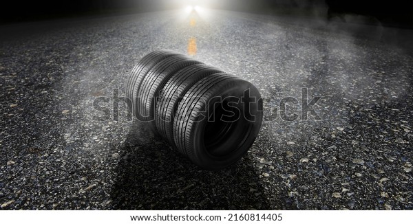 Car tyre on an asphalt road with\
smoke and a car headlight on the background at\
night
