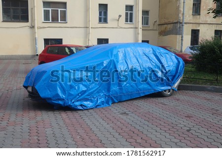 a car under a blue cape parked in the yard                                           