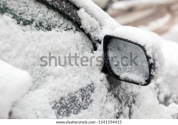 Car\
under the snow on the city street in winter day after cyclone or\
blizzard. Wet snow covered car mirror of parked\
car.