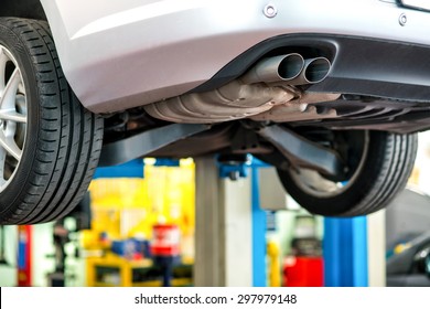 Car Undergoing Repair Or A Service In A Workshop Raised On A Lift Or Hoist With Focus To The Exhaust Pipe