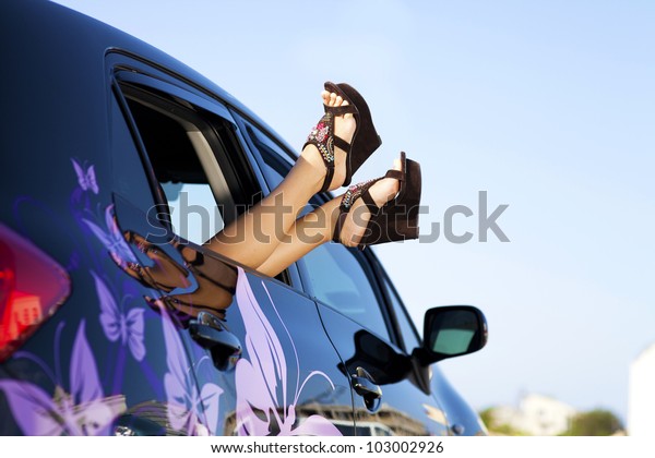 Car vacation\
holiday road trip. Travel and freedom happy lifestyle concept image\
of car with girl\'s feet during fun summer holidays. woman\'s legs\
with shoes in car window