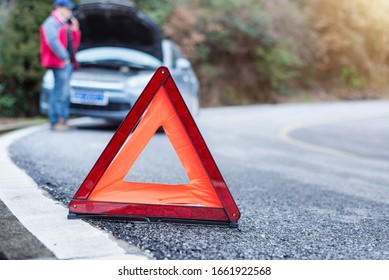 Car Warning Triangle On The Road Against The City In The Evening. Red Warning Triangle With A Car.