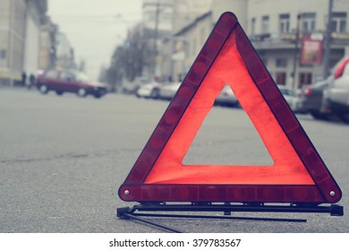 Car Warning Triangle On The Road Against The City In The Evening. Red Warning Triangle With A Car.