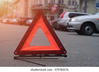 Car Warning Triangle On The Road Against The City In The Evening. Red Warning Triangle With A Car.