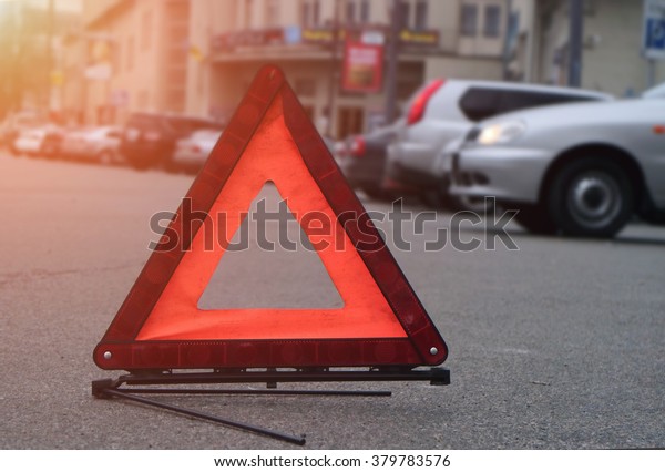 Car warning triangle on the\
road against the city in the evening. Red warning triangle with a\
car.