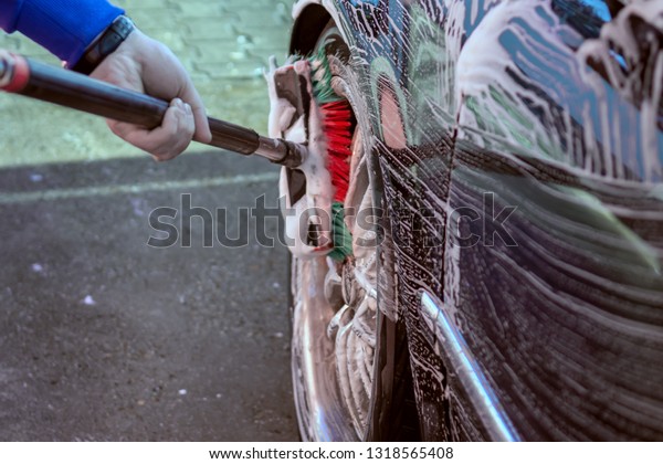 Car wash with a brush. The\
washer washes the wheels of a black car with a brush in the active\
foam