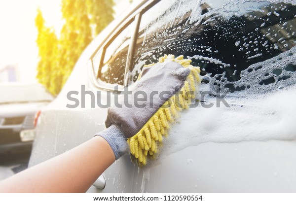 Car wash by\
hand. Soap suds, bubbles and Yellow mitt. Man washing windshield on\
white car by hand in hot\
day.